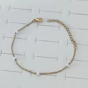 Detail shot of a gold stainless steel bracelet with delicate white enamel beads.