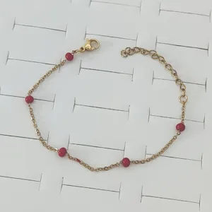 Detail view of a gold stainless steel chain bracelet featuring red enamel beads