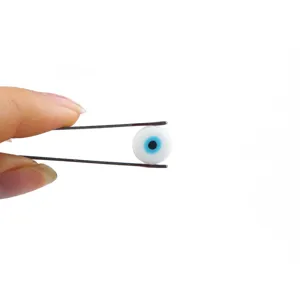 Macro view of a single white evil eye glass bead held by metal tweezers for DIY jewelry.