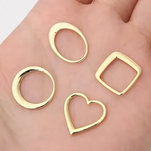 Vista macro detallada de dijes geométricos de corazón y óvalo bañados en oro de 14K en una mano