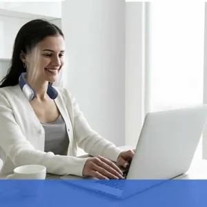 Woman using a portable leafless neck fan while working on a laptop in an office.