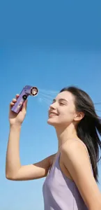Nahaufnahme eines lila tragbaren Mini-Handventilators im Freien unter strahlend blauem Himmel