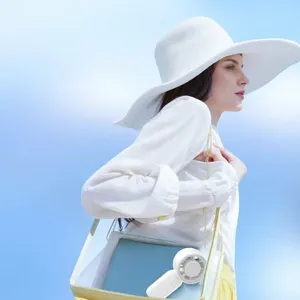 White mini portable handheld fan shown against a sunny outdoor lifestyle background