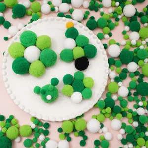 Kreative Anordnung von grünen und weißen Polyester-Pompons für DIY-Bastelarbeiten