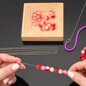 Close-up of hands using a stainless steel needle to string red beads for DIY jewelry making