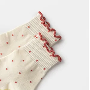 Detail of ruffled red edges and polka dot pattern on soft cream white knitted socks