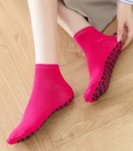 Nahaufnahme rosa Anti-Rutsch-Yogasocken mit schwarzen Gummigreifern auf Holzboden