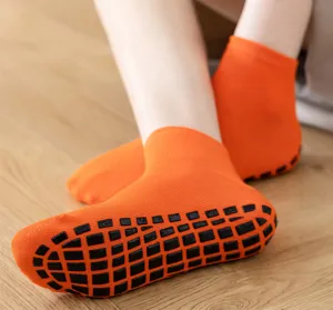 Detailaufnahme von orangefarbenen Anti-Rutsch-Socken mit schwarzen Gummigriffen auf Holz