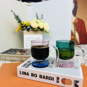 Unique floating colored borosilicate glass coffee cups with curved handles on books