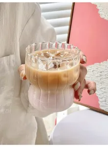 Close-up of hand holding striped glass cup with iced latte in aesthetic setting