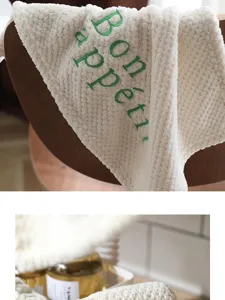 Close-up of "Bon appétit" green embroidery on soft off-white coral fleece hand towel.