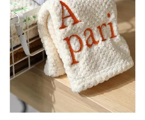 Close-up of white coral fleece kitchen hand towel with orange A pari embroidery.