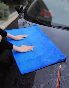 Primer plano de una toalla de microfibra azul secando agua en el capó de un coche