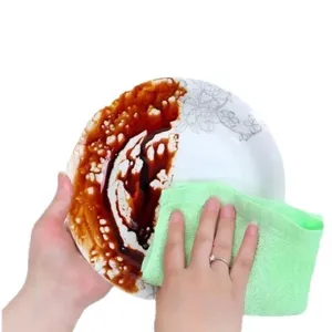 Green absorbent wood fiber dishcloth cleaning oil stains on a white ceramic plate