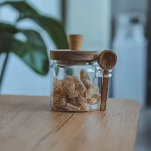 Detail view of a borosilicate glass seasoning jar featuring a wooden lid and a matching spoon