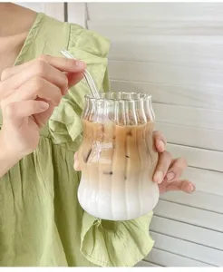 Nahaufnahme eines wellenförmigen Glasbechers mit Eiskaffee und einem gläsernen Strohhalm