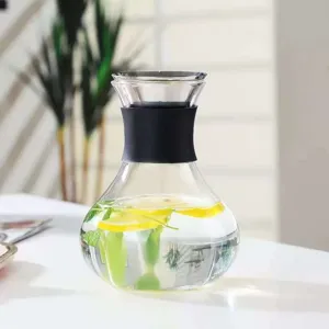Detailed view of clear glass cold water pitcher with black silicone grip and lemon slices inside.
