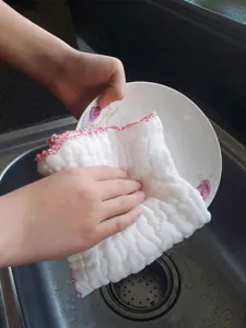 Close-up of thick cotton gauze dishcloth wiping a white ceramic plate in kitchen sink.