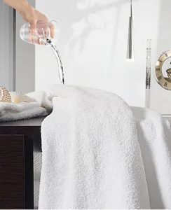 Close-up demonstration of water being poured onto a thick, absorbent white cotton towel texture