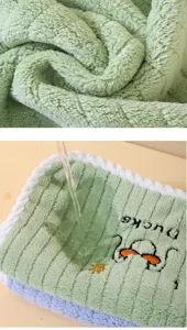 Close-up of soft green coral fleece towel with cute duck embroidery showing water absorption