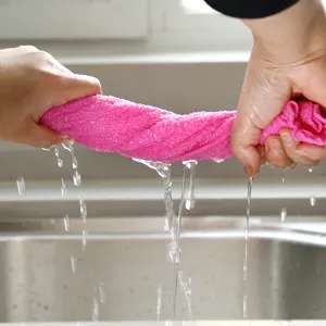 Close-up of pink wood fiber dishcloth being wrung out over a kitchen sink to show absorbency.