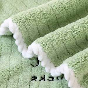 Macro view of soft green coral fleece towel texture with white scalloped edges detail.