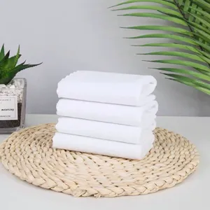 Detail view of four folded white absorbent cotton towels stacked on a straw mat.