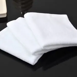 Close-up of three soft white cotton square towels stacked on black surface