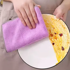 Close-up view of a thick purple microfiber dishcloth wiping oil stains off a ceramic plate