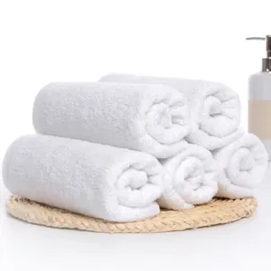Detailed view of multiple rolled pure white cotton hotel towels on a rustic woven mat