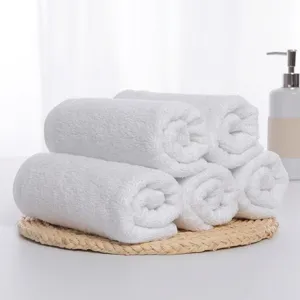 Six rolled white cotton towels neatly arranged on a natural woven mat for hotel bath