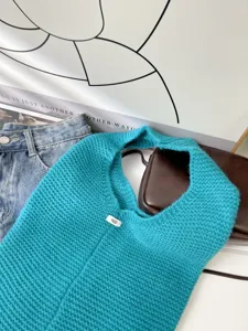 Close-up of a teal knitted tote bag with a soft woven texture and small egg label