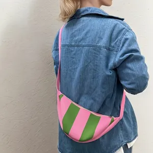 Back view detail of a pink and green striped crescent woven crossbody bag worn over denim