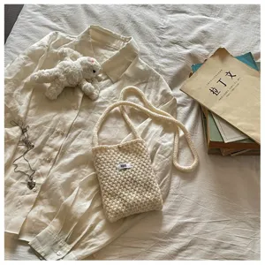 Close-up of a cream chunky knit crossbody phone bag featuring a minimalist egg tag detail