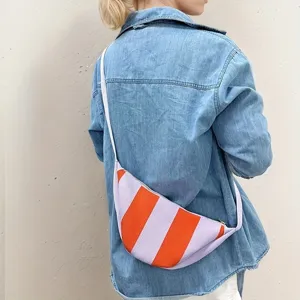 Detail of a striped purple and orange knitted crescent crossbody bag on a denim shirt.