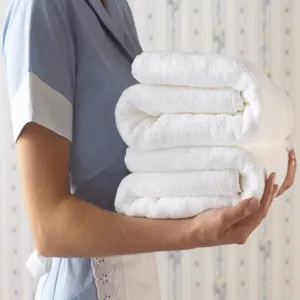 Close-up of premium thick white absorbent cotton bath towels held by professional hotel staff