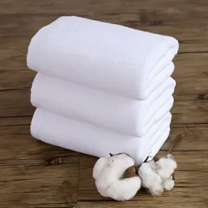 Set di tre asciugamani spessi in cotone bianco su fondo in legno rustico.