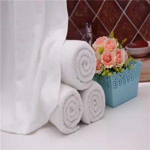 Premium soft white cotton bath towels rolled in a spa bathroom setting with pink roses