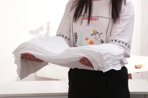 Detailed view of a thick stack of white absorbent disposable towels held by hands