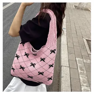 Detailed view of a pink knitted tote bag with black bow patterns worn on a shoulder.