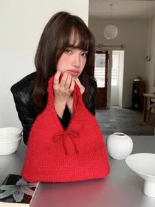 Red knitted handbag with bow detail held by model in minimalist indoor setting