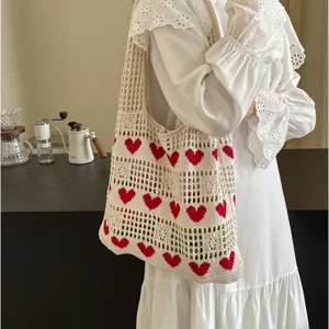 Detailed macro view of cream hollow knit tote bag featuring vibrant red heart patterns