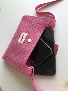 Detail shot of pink knitted crossbody phone bag with diamond pattern and brand tag.