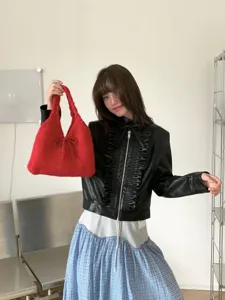 Stylish Asian model posing with a vibrant red knitted bow handbag in a minimalist studio.