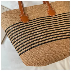 Detailed view of woven straw tote bag with black stripes and brown leather straps.
