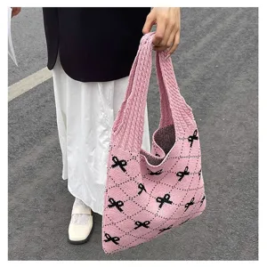 Close-up of a pink knitted tote bag with black bow patterns held by a woman outdoors