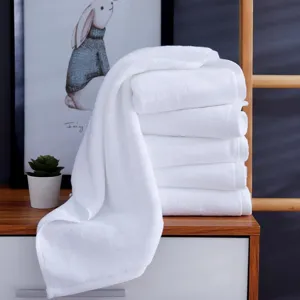Soft white cotton towels for hotel and salon use, neatly stacked on a wooden cabinet.
