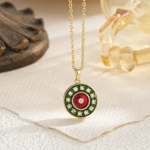 Close-up detail of a rotatable gold-plated Evil Eye pendant with green and red enamel.
