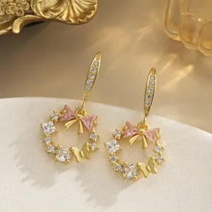 Elegant macro view of gold-plated wreath drop earrings with pink CZ bow and butterfly