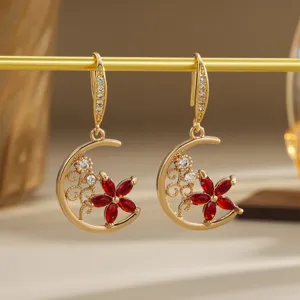 Macro view of gold crescent moon earrings with red crystal flower detail
